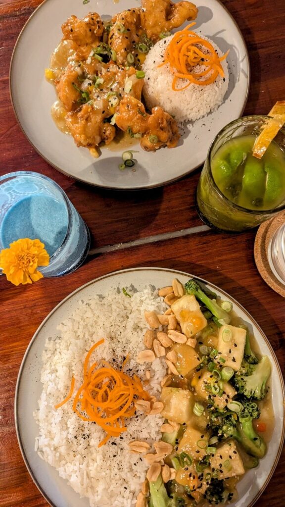 overhead shot with a plate of sweet and sour tofu with rice next to fried sweet cauliflower and rice with two colorful mocktails at Terrestre-Cocina-Compasion in san juan