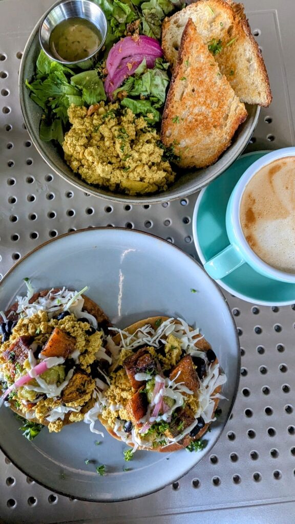 overhead shot with a plate with two vegan tostadas with roasted pumpkin and cashew cream next to a bowl with scrambled tofu and greens next to an oatmilk latte at berlingeri in san juan