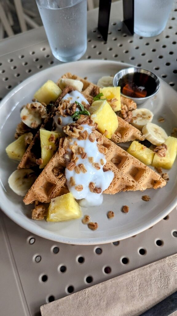 a stack of vegan golden belgian waffles covered in coconut yogurt, sliced bananas and pineapple chunks at berlingeri in san juan