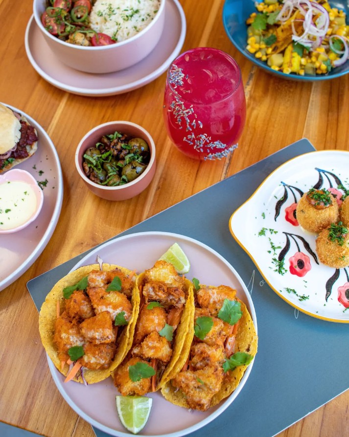 fried vegan cauliflower tacos, corn salad, and a pink drink spread across a wood table at flora vegan