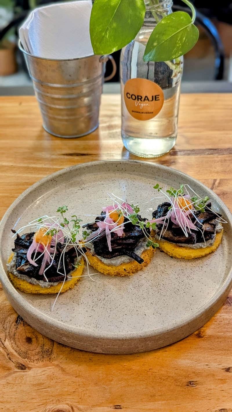 a round plate with three small arepas topped with eggplant and tofu ricotta at coraje vegan in medellin