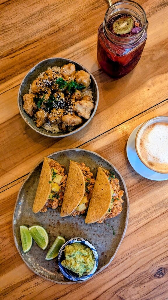 overhead shop of fried vegan orange caulifower and tacos pastor on a wood table with coffee and tea at kaime restaurant in medellin