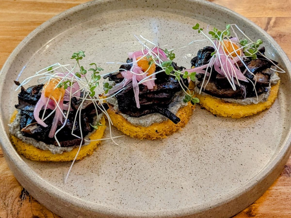 a round plate with three small arepas topped with eggplant, mushrooms and tofu ricotta at coraje vegan in medellin