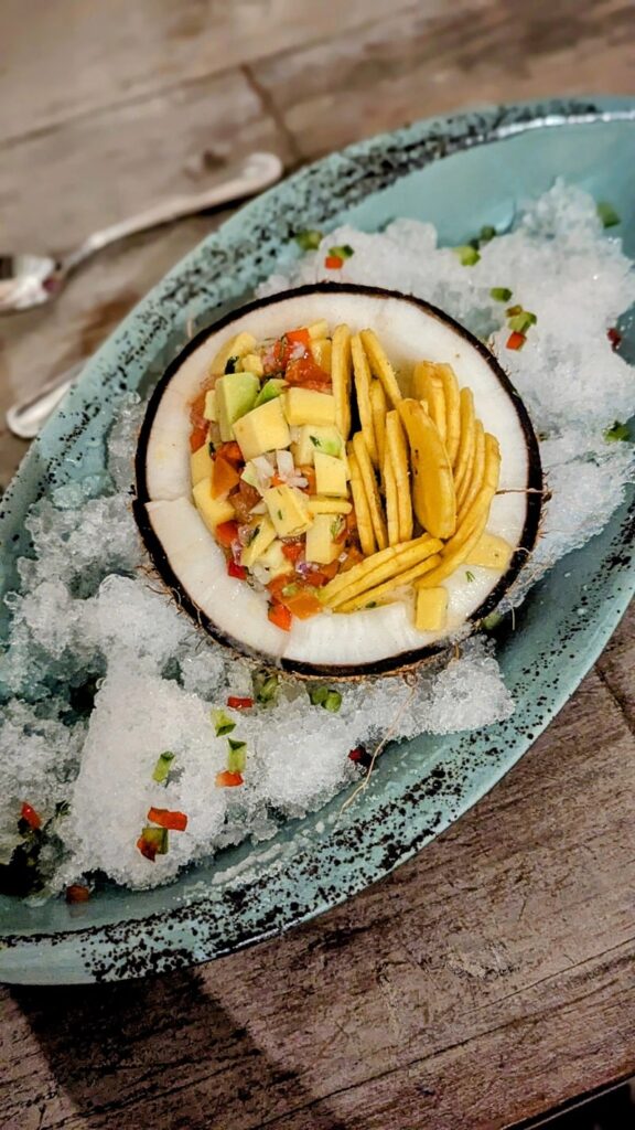 a small round coconut filled with vegan ceviche and plantain chips on a platter with shaved ice at cande cocina in cartegena