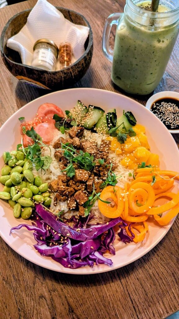 large bowl filled with colorful chopped vegetables and tempeh next to a green smoothie at coco bowl in salento, colombia