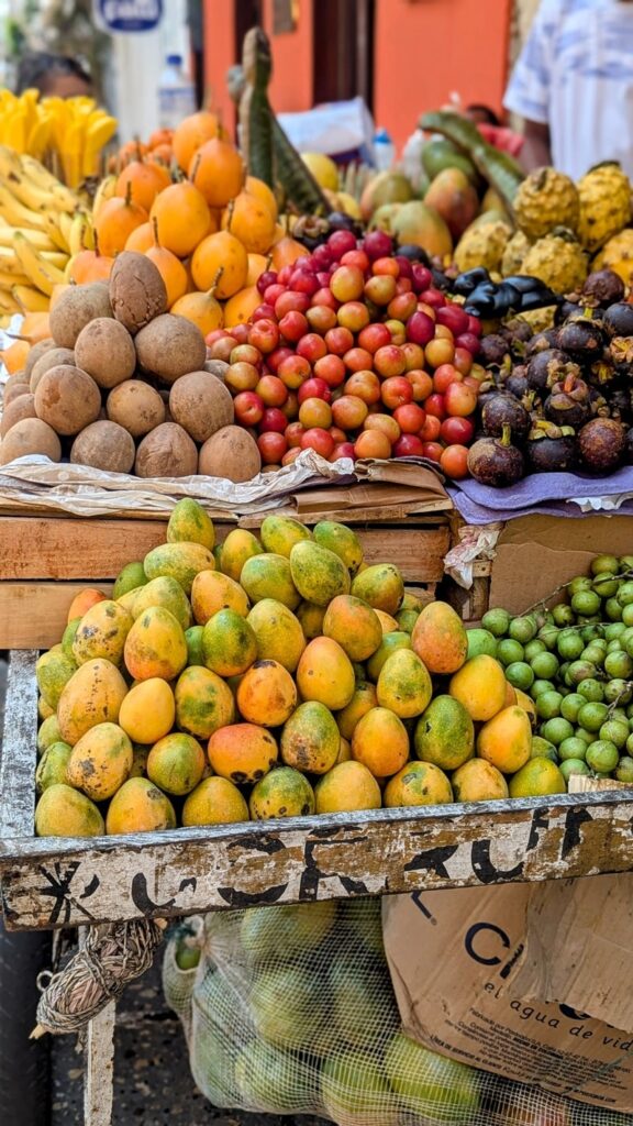 a tall fruit stand with pyramids of colorful yellow, green, and red fruits in colombia