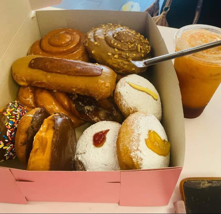 a pink card board box filled with a variety of vegan donuts next to an iced coffee at ronalds donuts in las vegas