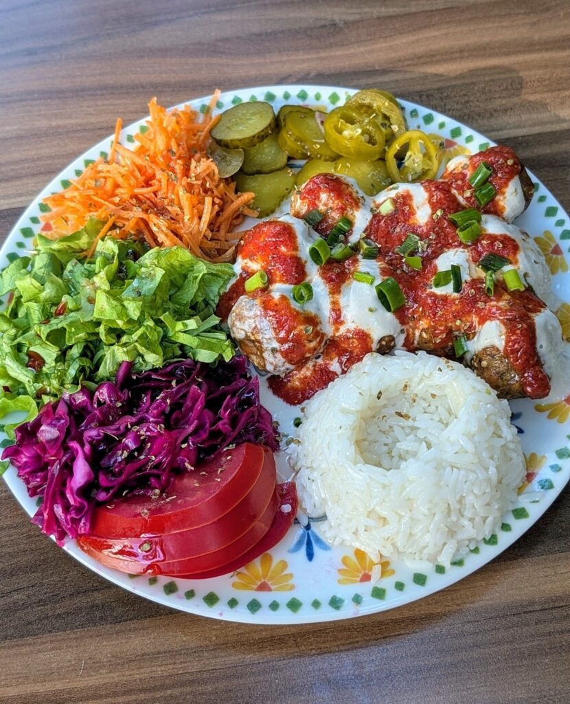 a plate of vegan meatballs covered in a cashew yogurt sauce with salad and pickled veggies at Veganarsist in istanbul