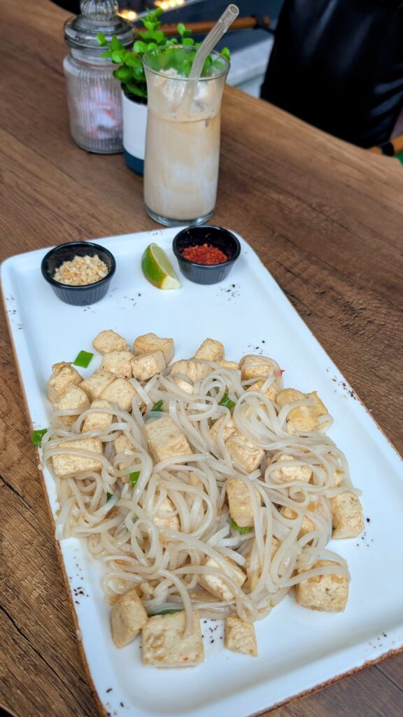 a rectangle plate with a pile of rice noodles mixed with fried tofu next to a coconut cold brew coffee at Asian Vegan Kitchen