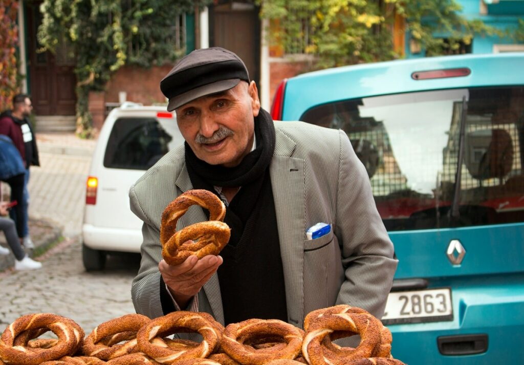 old man in a gray suit jacket holding a round turkish sesame bread