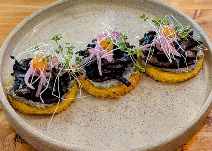 three small round vegan corn arepas topped with mushrooms and pickled vegetables in medellin colombia