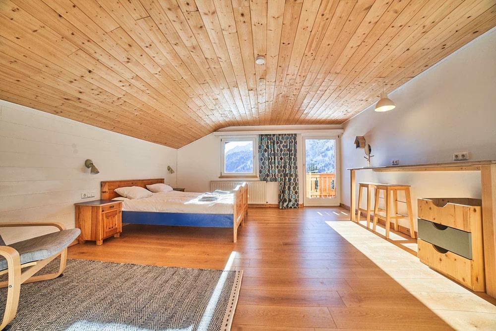 inside of a bright guestroom at the vegan friendly ski resort moaAlm Mountain Retreat. the room has light wood floors and ceiling with a large bed 