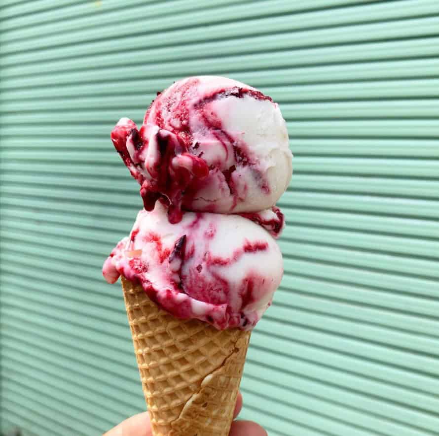 two scoops of vegan berries and cream ice cream on a cone in front of a mint green door in berlin