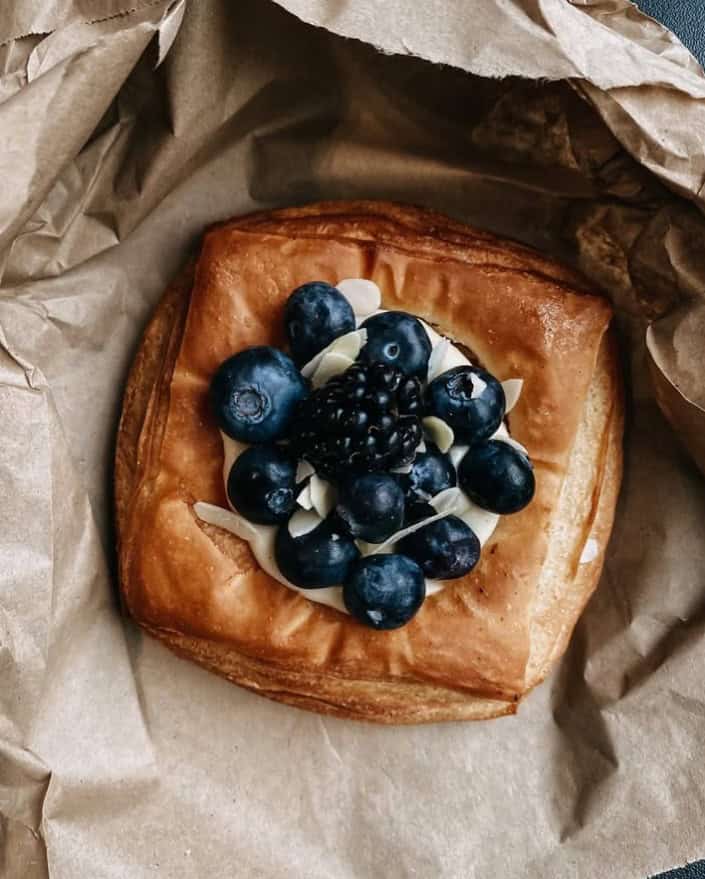 a single golden vegan pastry topped with cream and blueberries in a brown paper package at the vegan bakery sanctuary in berlin