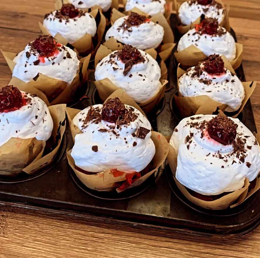 three rows of vegan chocolate cupcake topped with a mound of white cream, a cherry and a dusting of chocolate from the vegan bakery and cafe velicious in berlin