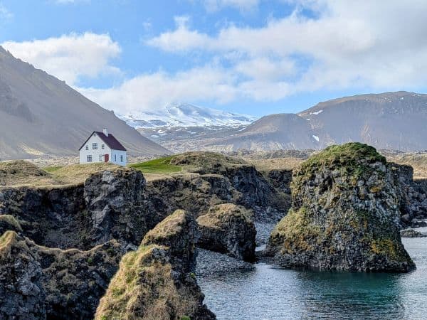 a small white house in the middle of rural iceland surrounded by water on one side and mountains on the other 