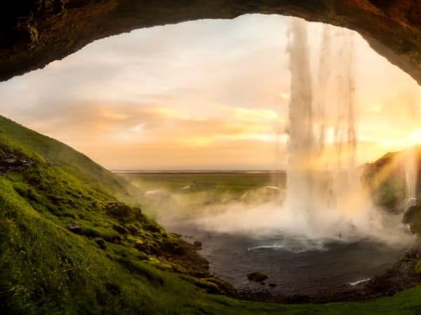 behind a waterfall as the sun sets in iceland