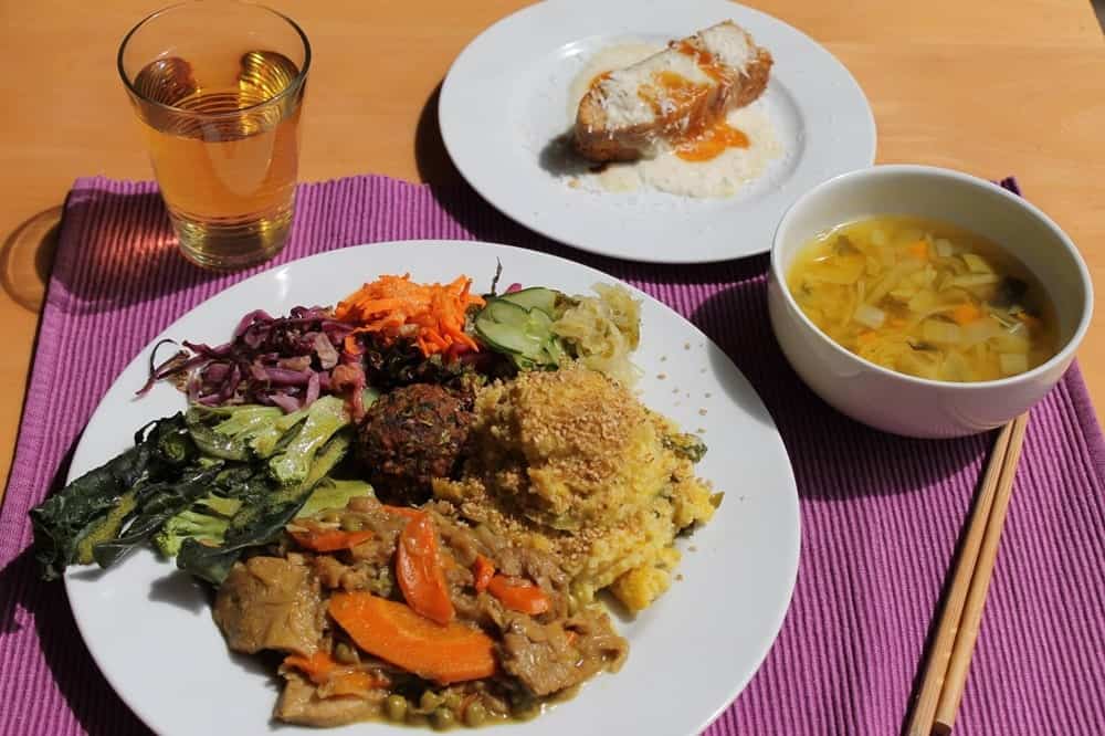 a large whiet plate filled with mixed veggies next to a bowl of soup and a dessert at Cozinha Consciente in coimbra