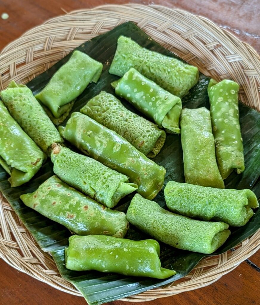 vegan pandan pancake rolled tightly around a filling of grated coconut that’s been simmered in palm sugar until it’s sticky and rich with brown caramel
