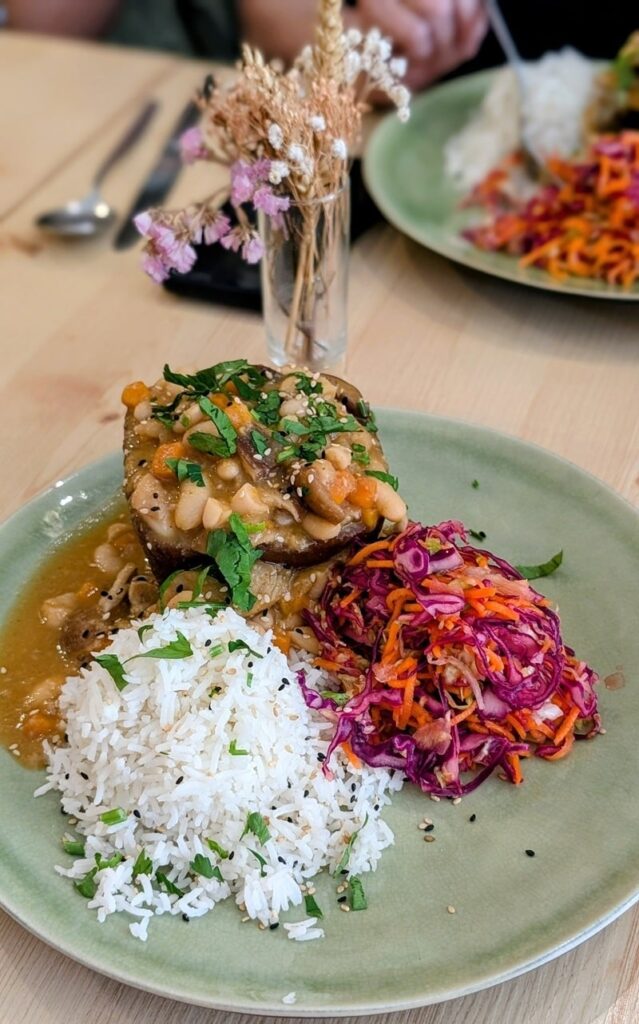 a round green plate filled with a vegan portugese rice and bean stew, white rice, and cabbage salad at o Macrobiotico in porto