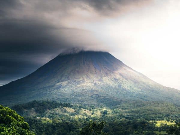 the arenal volcan surrounded by a thick mist with a little sunlight peeking through in costa rica