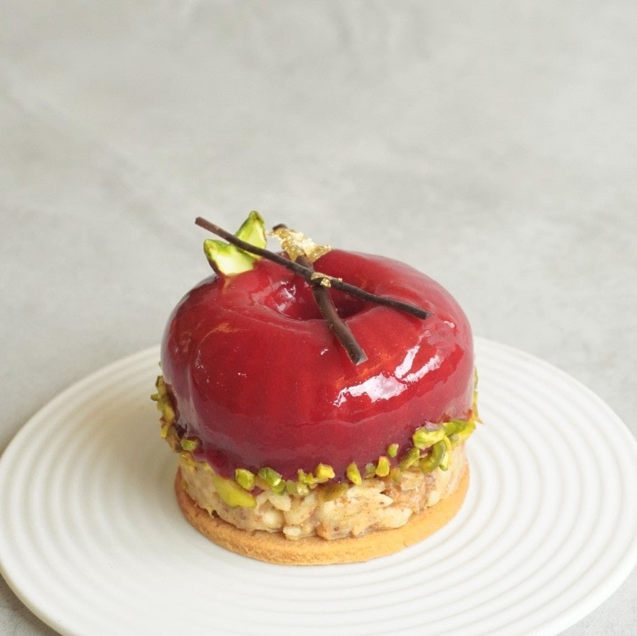 a vegan chocolate pastry covered with nuts at the base and then topped with a red glazed fruit on a white plate from greendot in singapore