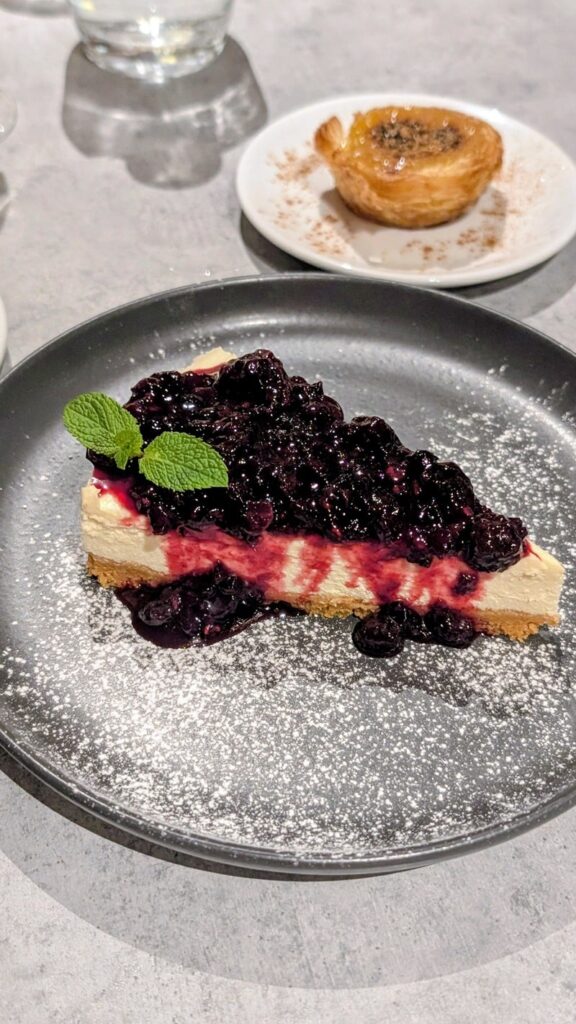 vegan cheese cake topped with a berry compote and a vegan pastel de nata behind it at the kind kitchen in porto