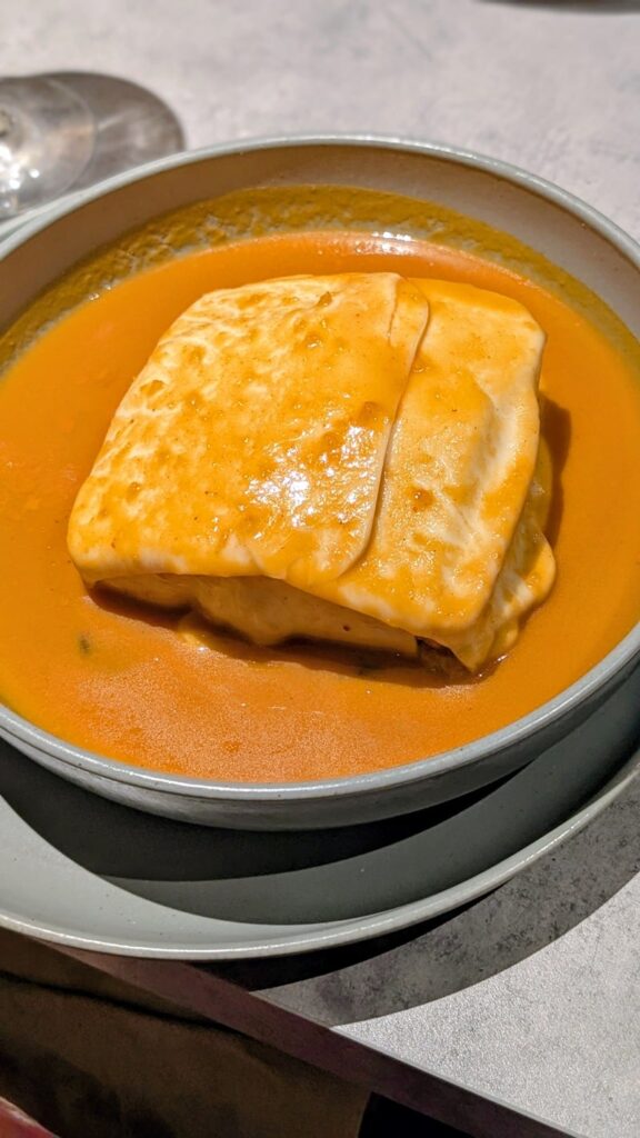 vegan Francesinha, a hearty dish with layers of cheese and bread in a thick broth at kind kitchen in porto