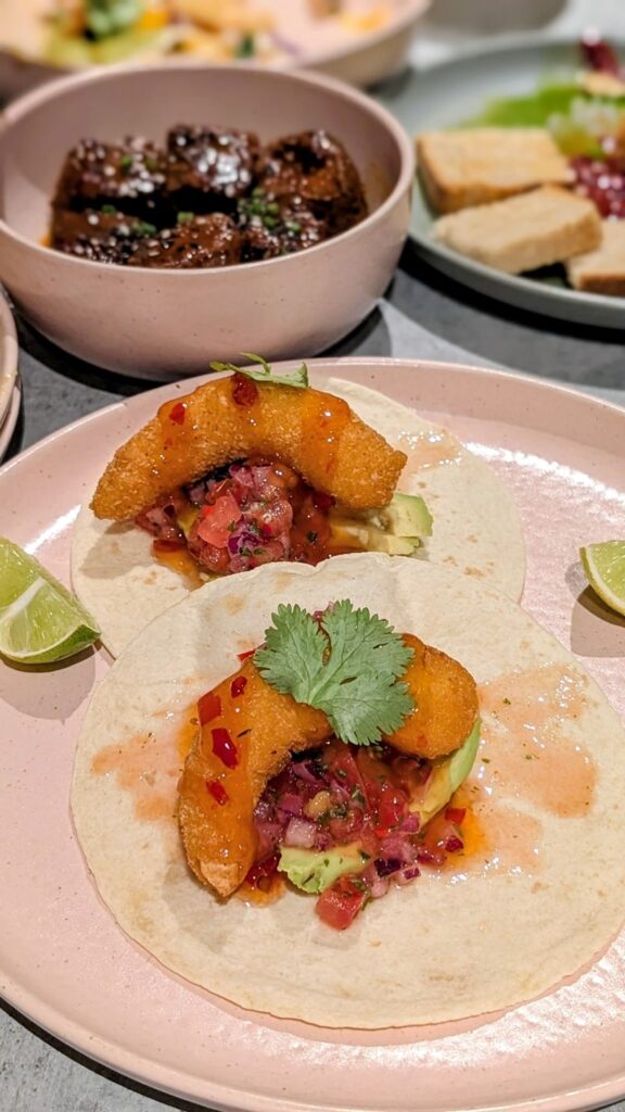 two colorful vegan shrimp tacos in front of a bowl of fried chick'n nuggets at kind kitchen in porto