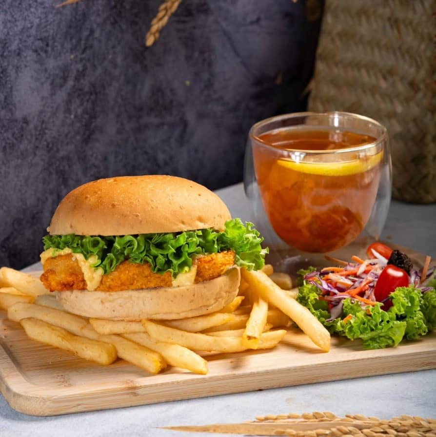 large vegan fried chick'n burger with golden french fries and a drink on a wood tray from nomvnom