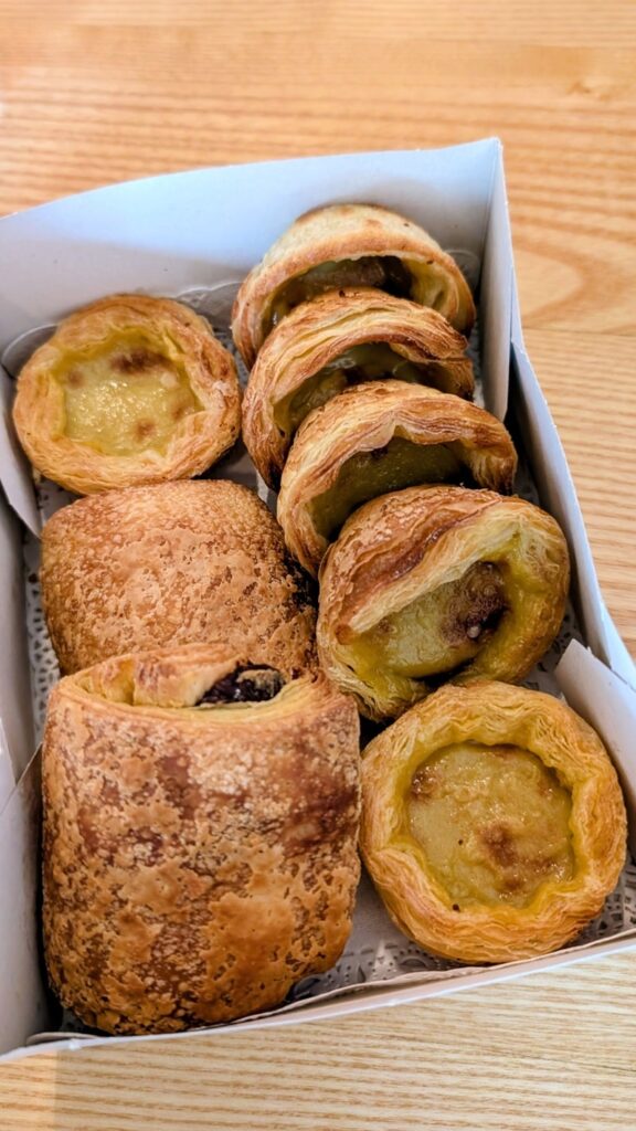a white to go box filled with six vegan pasteis de nata and two vegan chocolate croissants from odete vegan bakery