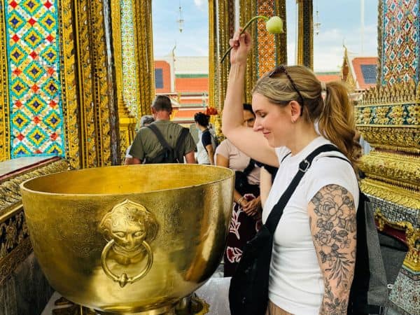 a woman dipping a flower into water in a temple in thailand for a blessing