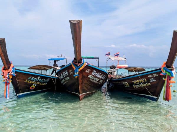three large wooden thai boats sitting docked on a beach