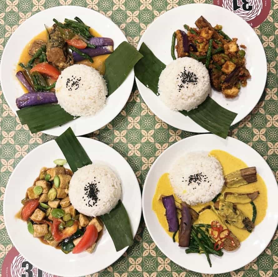four different vegan curry and stirfry dishes spread across a green and white table at warung ijo in singapore