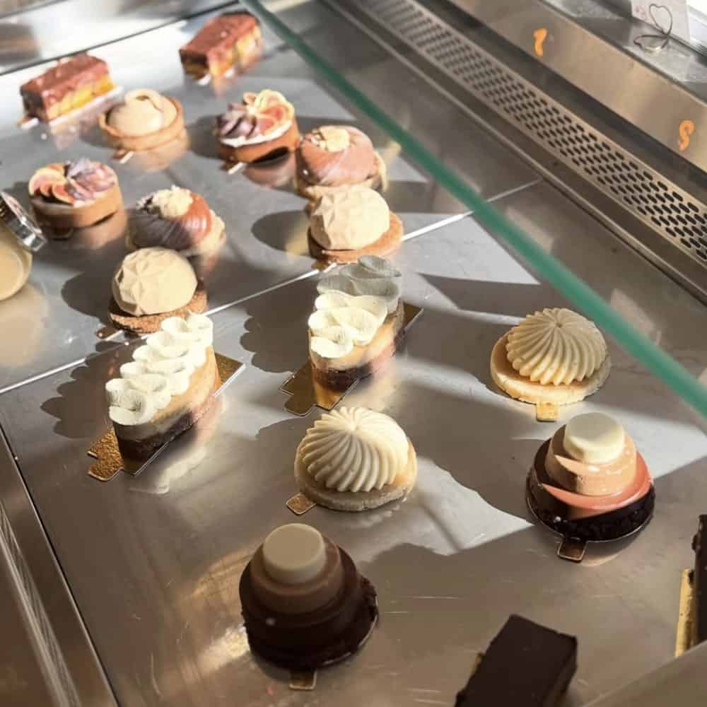 a pastry case filled with individual housemade vegan pastries topped with cream and chocolate at amour in nice france 