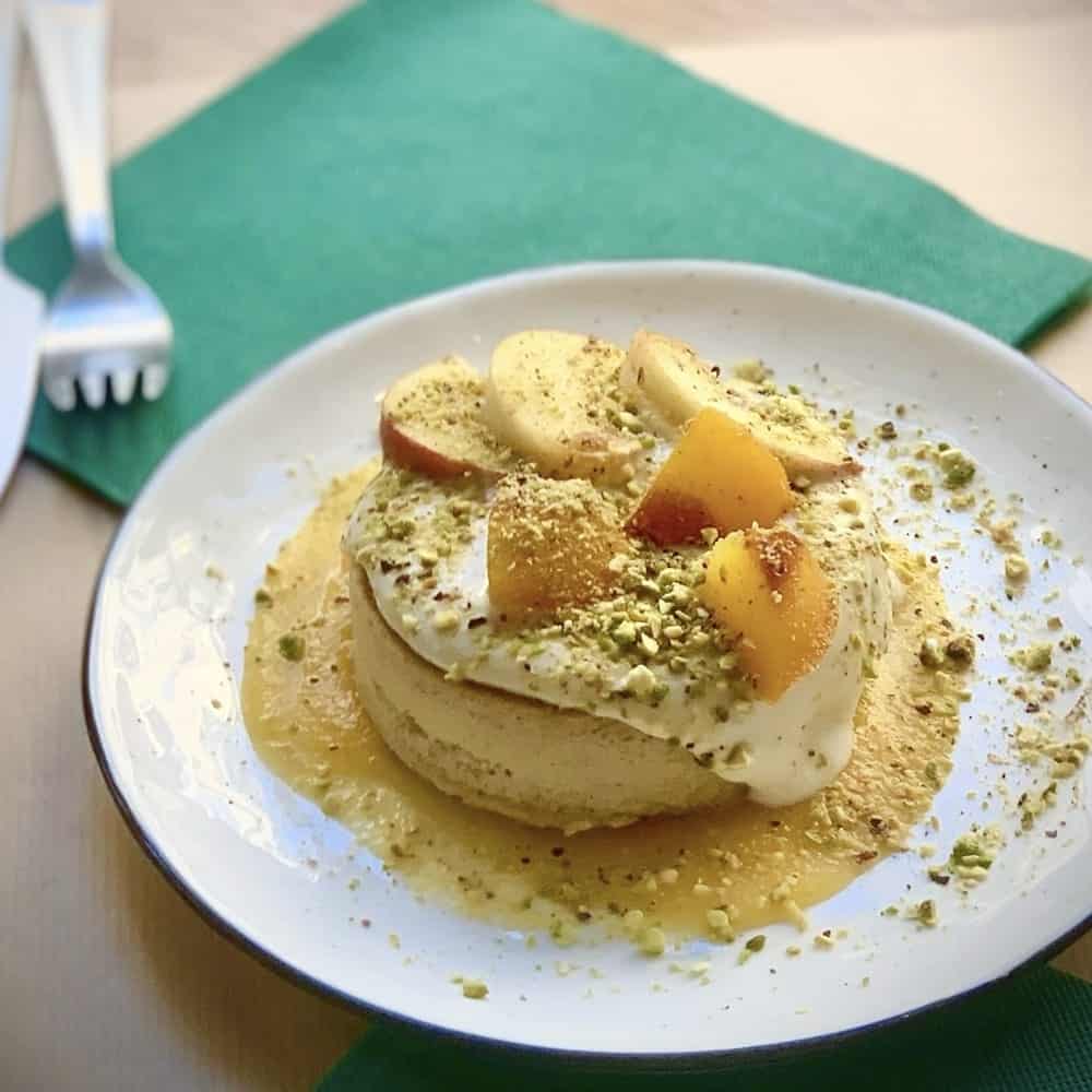 a stack of golden vegan pancakes topped with cream and sliced pears at paper plane in nice france