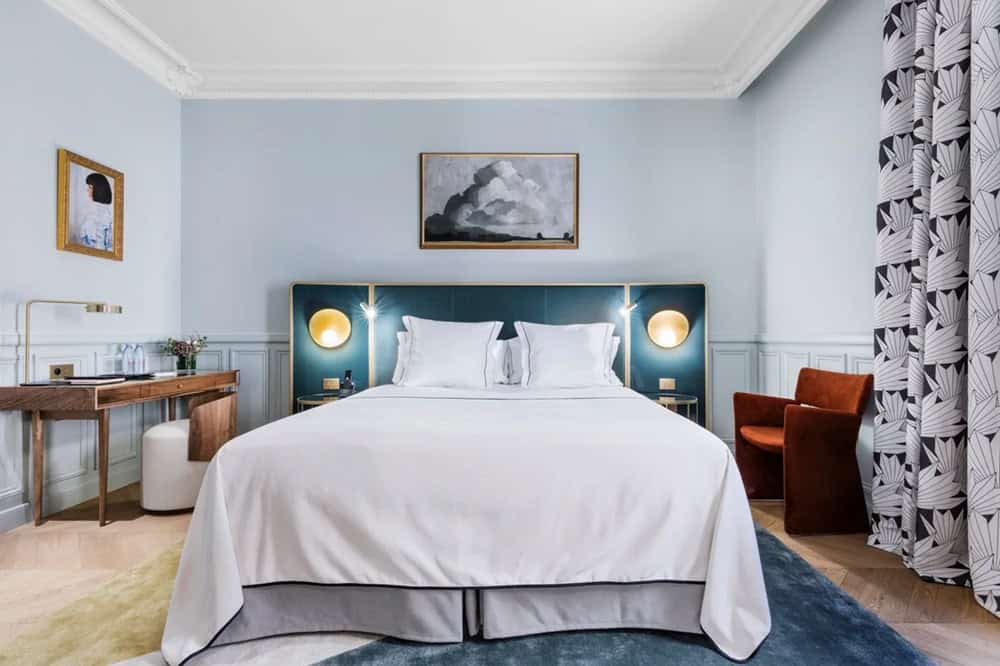 inside of a chic and sophisticated guest room with white linens and vibrant colored accents at the grand powers hotel in paris