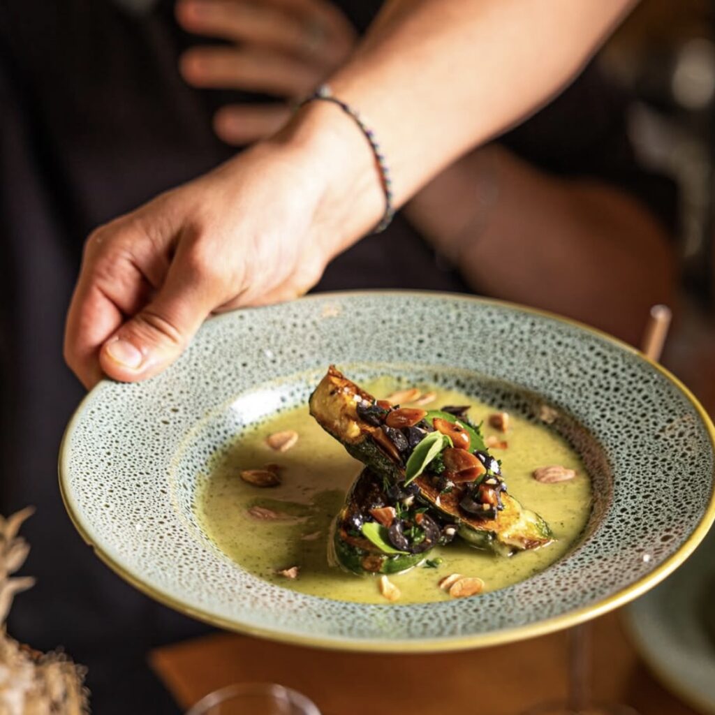 a light blue bowl with a creamy yellow broth with a veggie creation in the middle at Laska