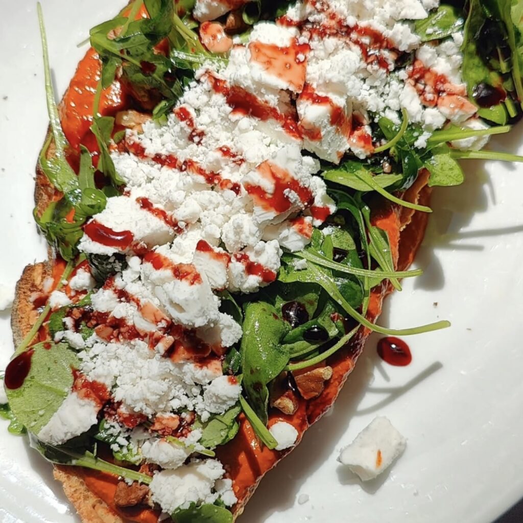 a bed of greens topped with a white cream sauce and a red pepper sauce at ZEITGEIST.