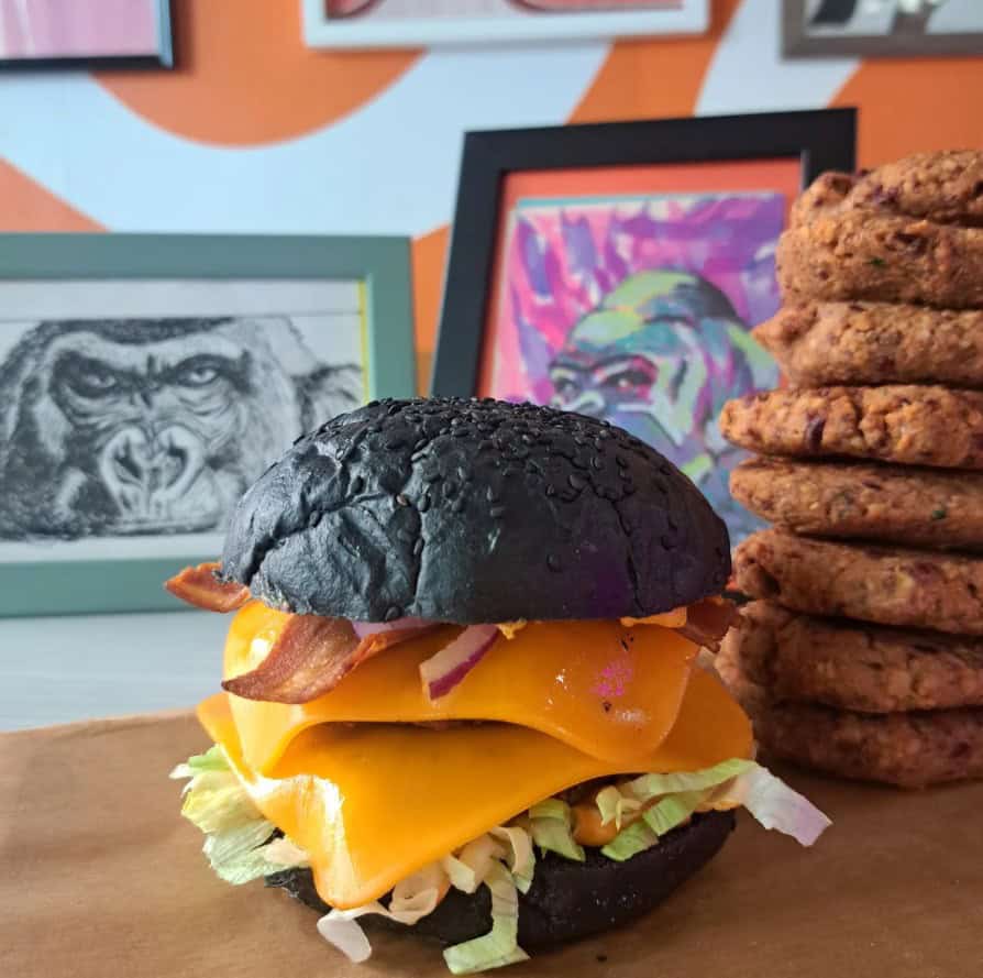 a giant vegan burger with a black charcoal bun and slices of cheese next to a stack of cookies at junga