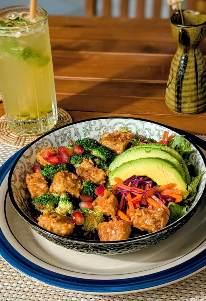 vegan miso peanut tempeh and veggies with sliced avocado and a light yellow drink at ojas in siem reap