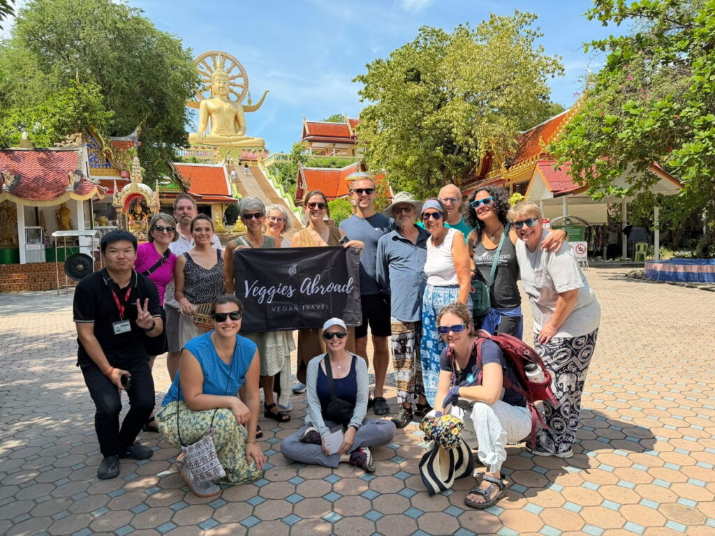group of veggies abroad travelers holding a banner in front of a temple on koh samui