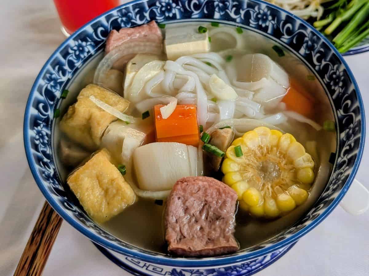 up close shot of a vegan noodle soup with rice noodles, chunks of corn and tofu in Phnom Penh