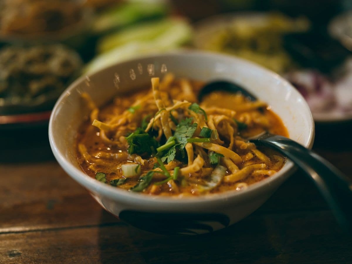 a bowl of vegan khao soi with a spoon off to the side on a wood table in phuket thailand
