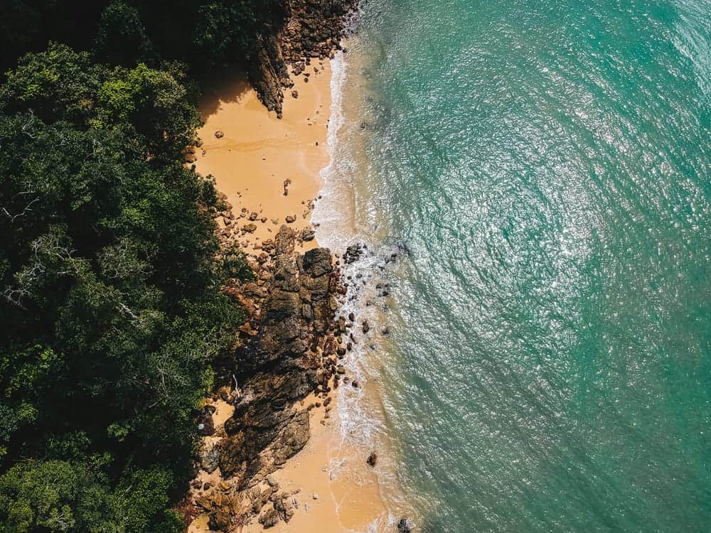 overhead shot of a secluded, beautiful beach with turquoise water and lush green forest on Koh Phayam in thailand