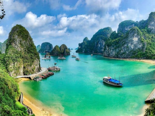 a bright and clear day in halong bay with bright green water surrounded by large rock formations