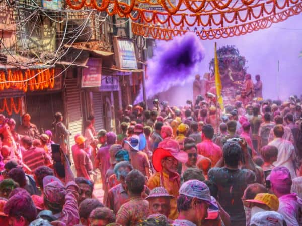people crammed into a street during the holi festival with a large purple plume of color in the air