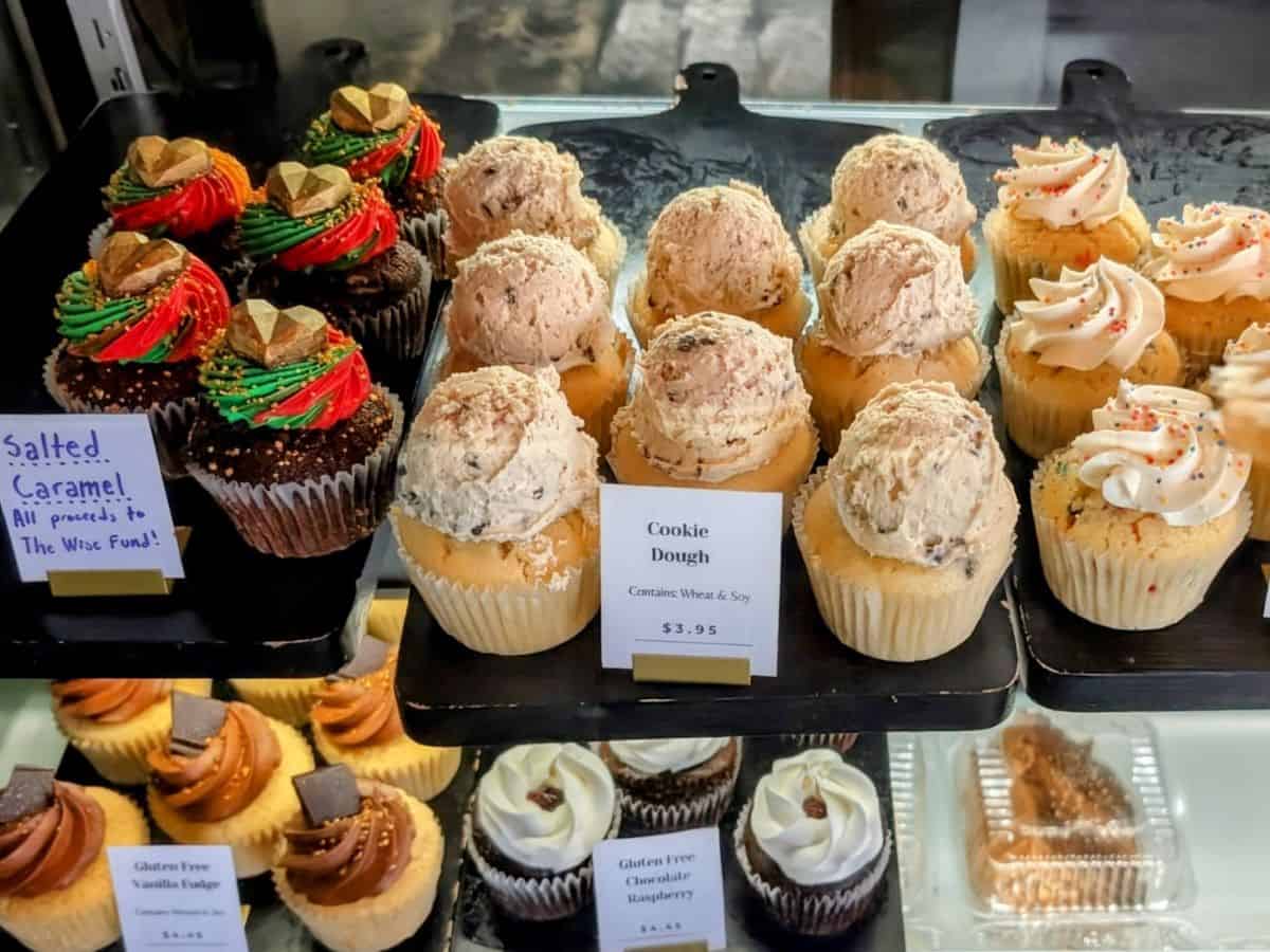 a bakery case filled with rows of vegan cupcakes topped with swirls of colorful frosting and scoops of cookie dough at vegan east bakery in minneapolis