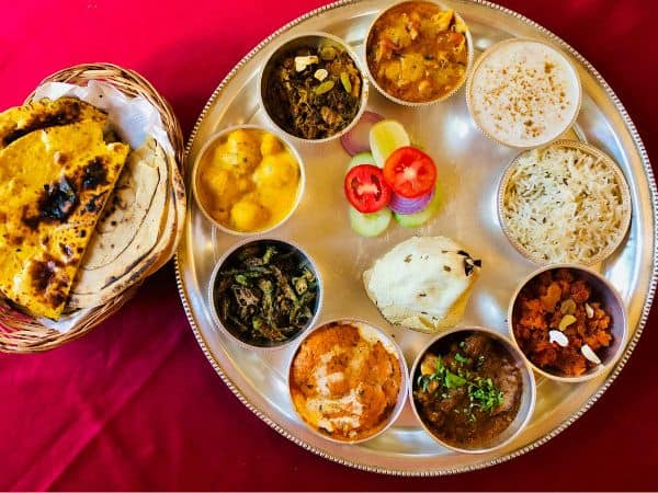 a platter with mini dishes on top filled with vegan indian food nest to a basket with bread