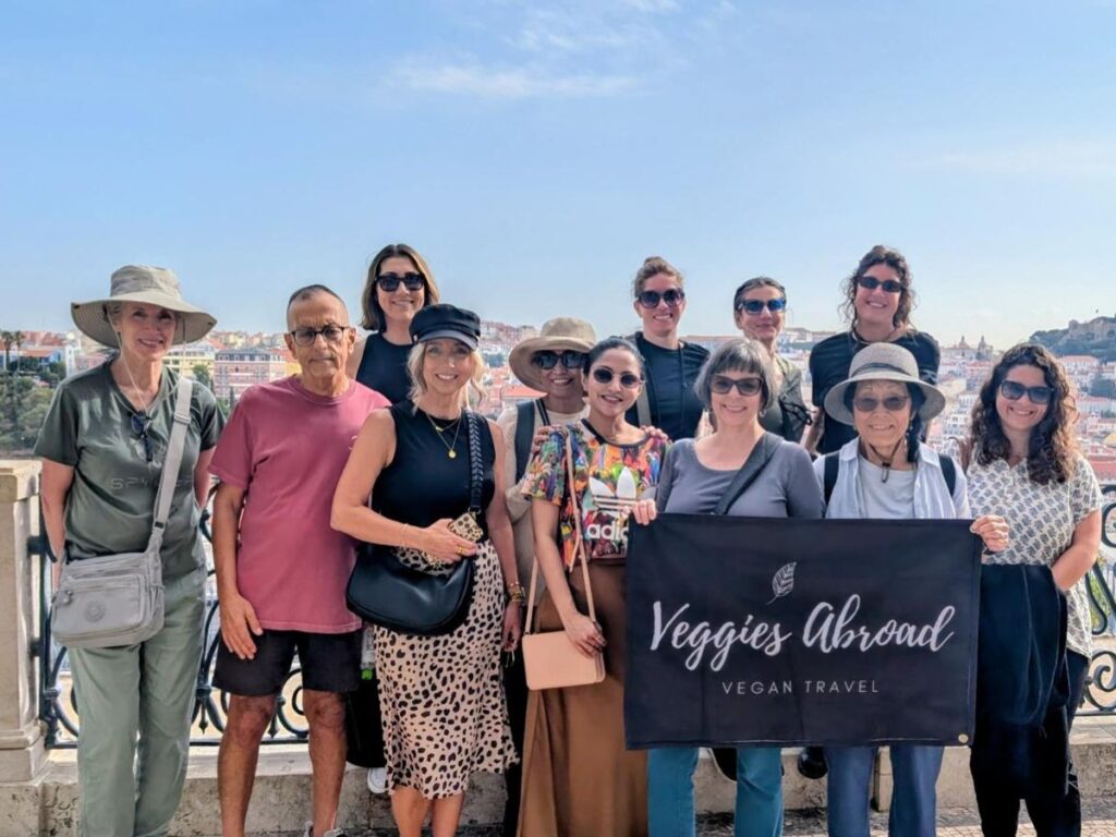 group of travelers in portugal holding a sign that says veggies abroad vegan travel in portugal